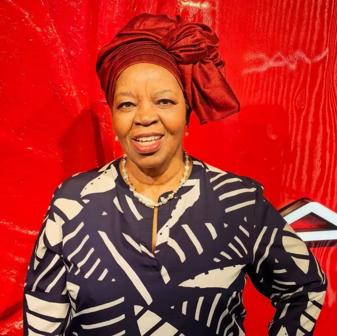 Professor Sheila Tlou smiling in front of a red background.